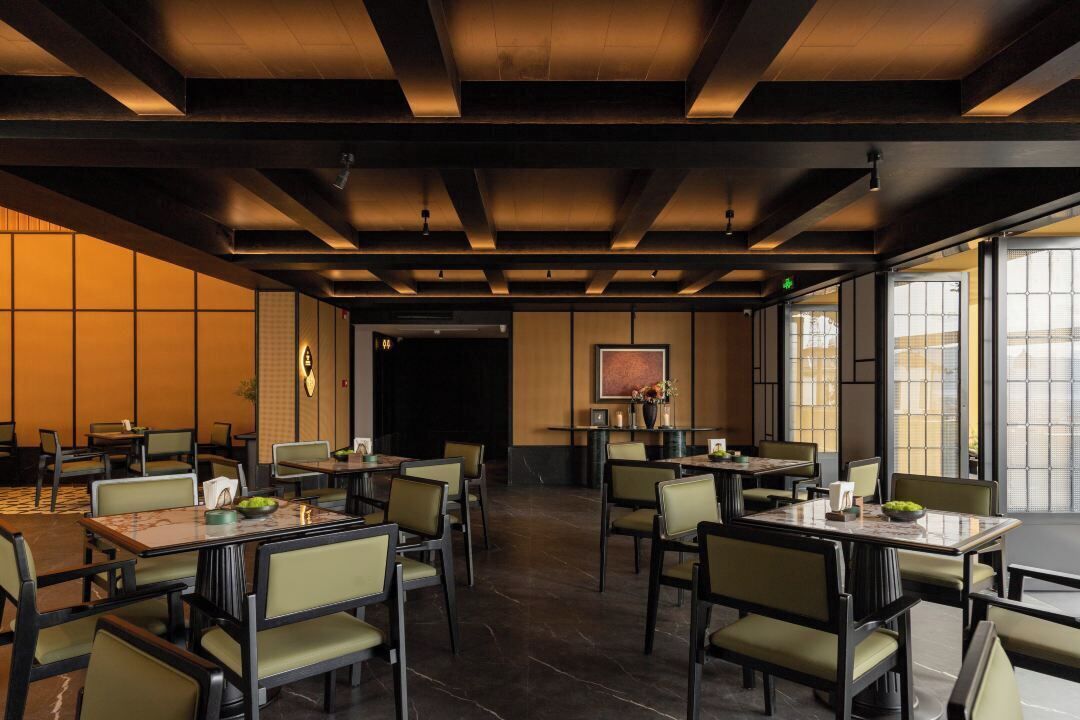 A restaurant with multiple tables and chairs, a tiled floor, and a large window on the right side.