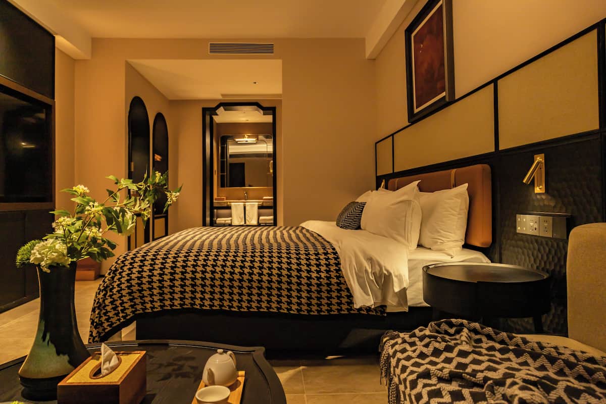 Ein Hotelzimmer mit Bett, Nachttisch, Lampe und einer Topfpflanze.