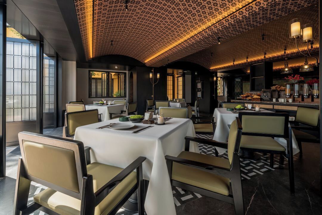 Un comedor moderno con mesas dispuestas para cuatro, destacando un techo con diseño geométrico y sillas contemporáneas.