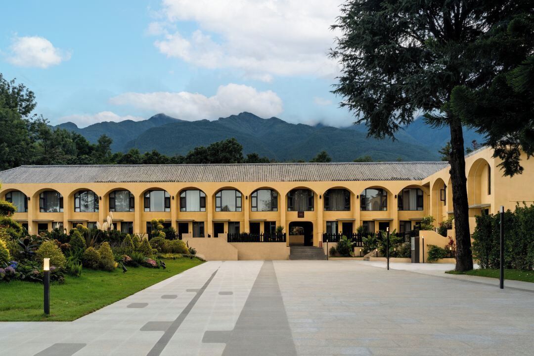 A building with a long central corridor, arched windows, and a mountainous backdrop.