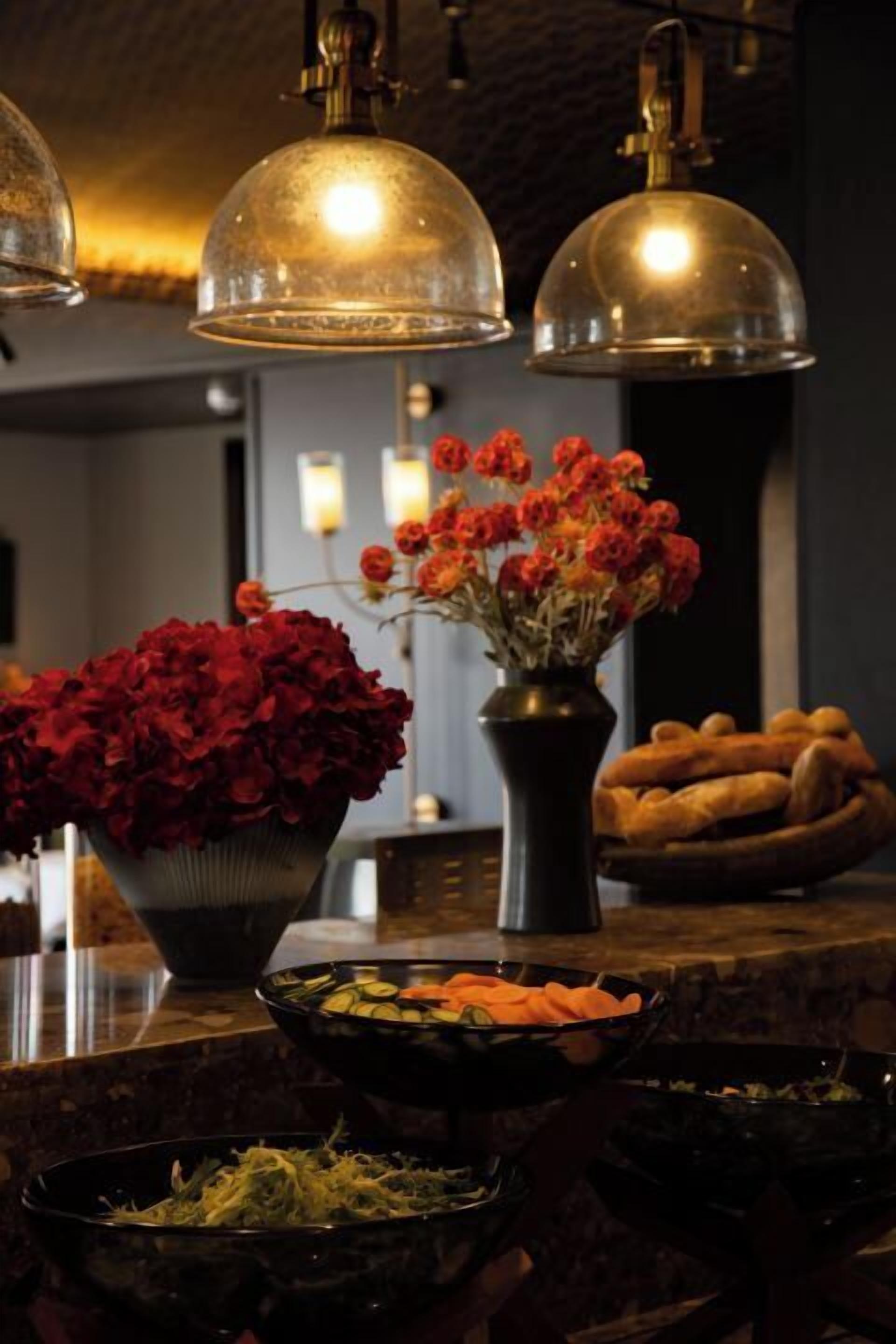 A bar area with a bowl of red flowers, a vase of orange flowers, and a bowl of sliced vegetables.