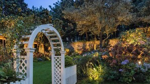 Un jardín con un arco blanco y un edificio de estilo pagoda al fondo.