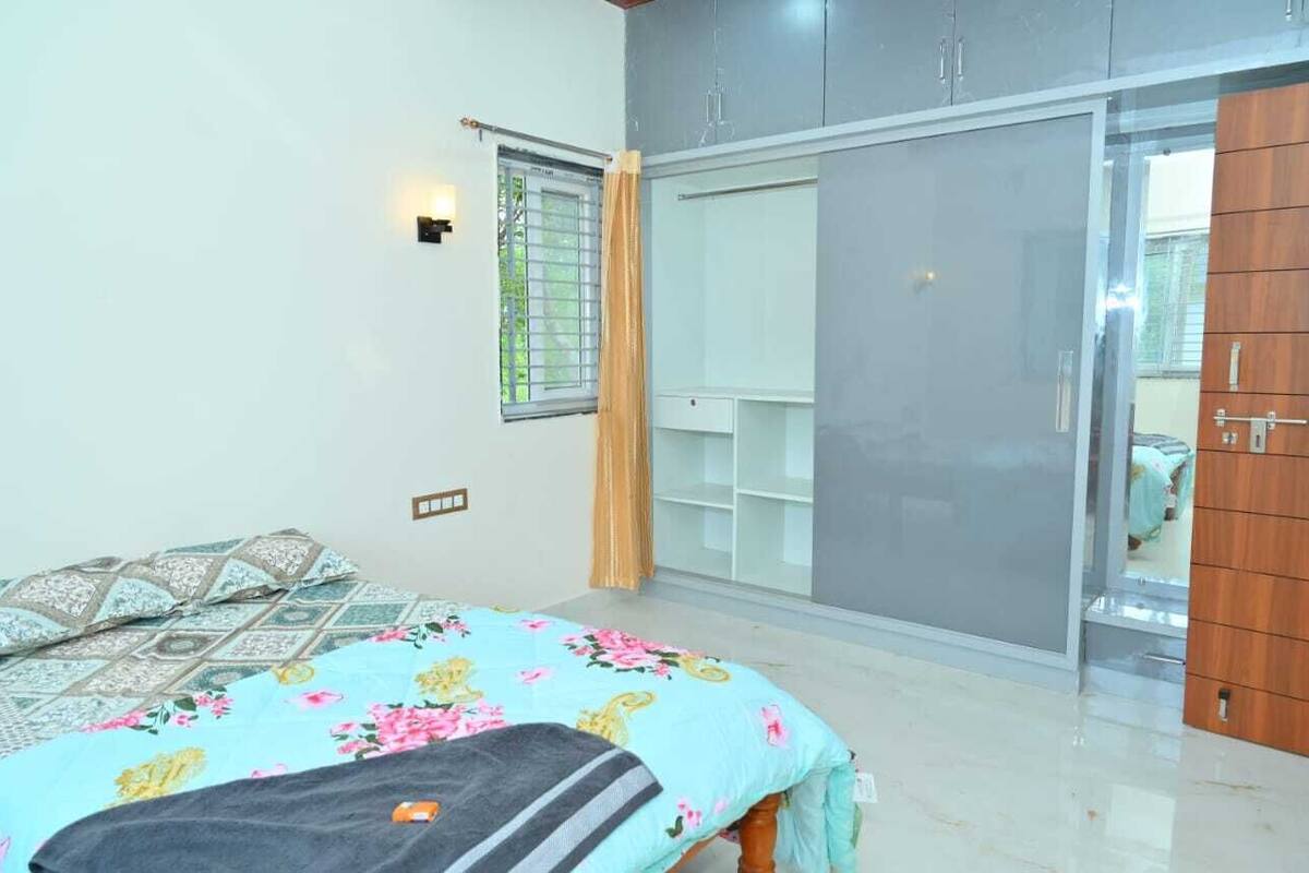 A bedroom with a bed, a wardrobe, a mirror, and a window with curtains.