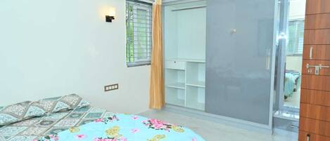 Um quarto com cama, guarda-roupa, espelho e janela com cortinas.
