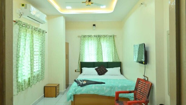 A bedroom with a bed, a chair, an air conditioning unit, a ceiling fan, and a television. - Radha Krishna Heritage  (Hospet)