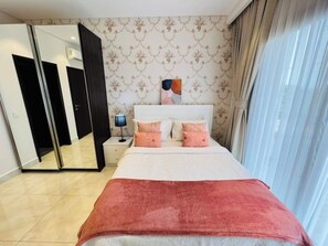 A bedroom with a bed, a nightstand, a lamp, a mirror, and a wardrobe. - Elegant 2BR Luxury Apt•Modern, Cozy, Airport Pool, Mirage , Accra  (Accra)