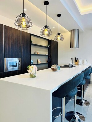 Una cocina moderna con una isla central, taburetes de bar, iluminación colgante y una campana extractora de acero inoxidable.