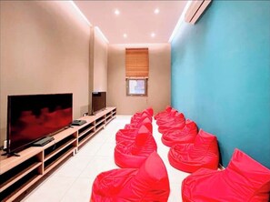 A room with a TV, wooden entertainment unit, and red bean bags arranged in rows. - Elegant 2BR Luxury Apt•Modern, Cozy, Airport Pool, Mirage , Accra  (Accra)