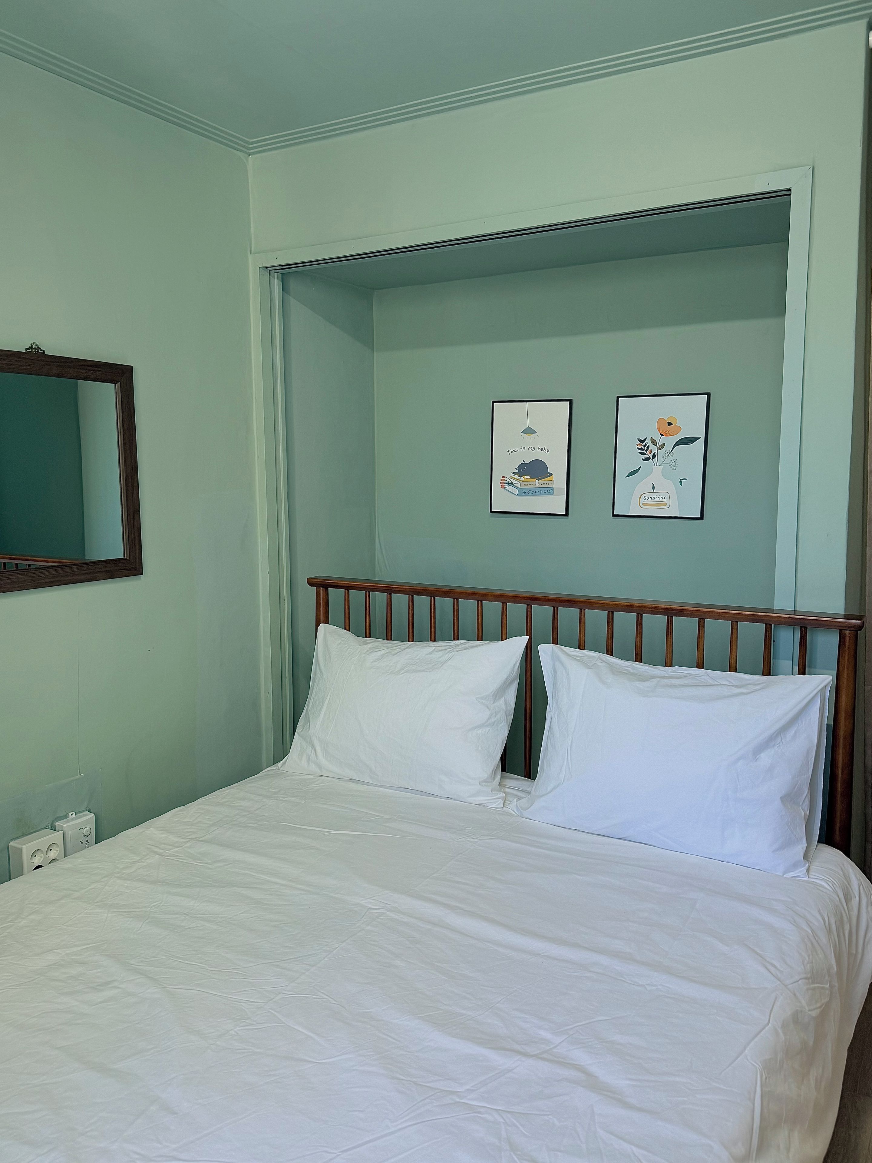 A bed with white bedding, a wooden headboard, and two framed pictures on the wall.