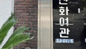 A hotel entrance with a sign indicating room number 12-1, a blue sign for a CESCO Members store, and a visible hotel sign in Korean. - Mint Stay (Jeju City)