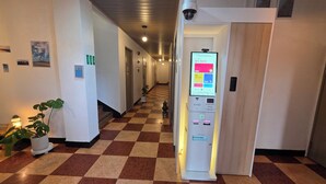 Un couloir d’hôtel avec un sol à carreaux, un comptoir de réception doté d’un écran numérique et une caméra de surveillance.