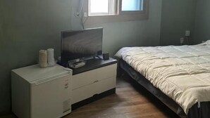 A bedroom with a bed, a TV on a stand, a small white cabinet, and an air conditioning unit. - Mint Stay (Jeju City)