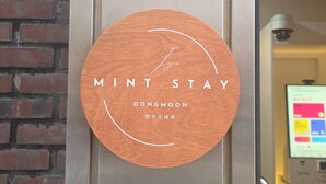 Une enseigne en bois portant les inscriptions « MINT STAY » et « DONGMOON », indiquant un hôtel ou un établissement proposant des hébergements.