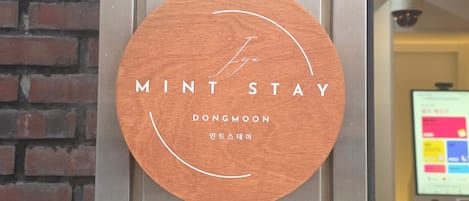 Een houten bord met de tekst 'MINT STAY' en 'DONGMOON', wat een hotel of accommodatie aangeeft.