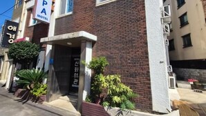 A two-story building with a sign for 'PUSPA MOTEL' on the left. There are potted plants in front of the entrance. - Mint Stay (Jeju City)