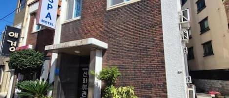 En toetagers bygning med skilt for 'PUSPA MOTEL' til venstre. Der er plantekasser med blomster foran indgangen.