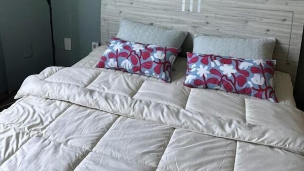 A neatly made bed with white bedding and floral-patterned pillows, a bedside lamp, and a framed picture on the wall. - Mint Stay (Jeju City)