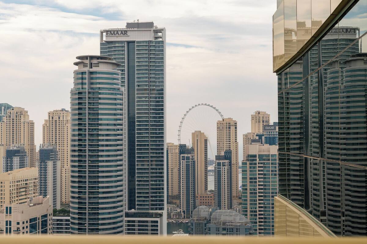 Eine Stadtansicht mit modernen Hochhäusern, darunter ein markanter Emaar-Turm, und einem Riesenrad im Hintergrund.