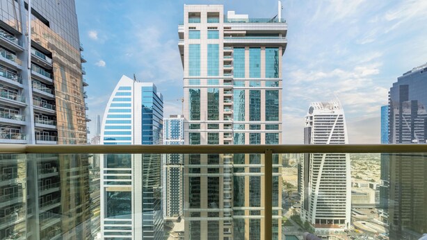 Un immeuble de grande hauteur doté d’une façade moderne en verre, vu depuis un balcon orné d’une rambarde en métal.
