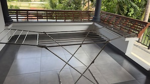 A balcony with a metal drying rack, tiled floor, and a view of greenery.