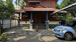A two-story house with a tiled roof, a porch with columns, and a car parked in front.