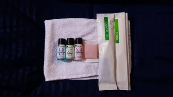 A white towel with three bottles of body wash, shampoo, and moisturizer, and a dental kit on a dark blue fabric.