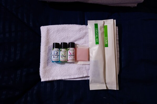 A white towel with three bottles of body wash, shampoo, and moisturizer, and a dental kit on a dark blue fabric.