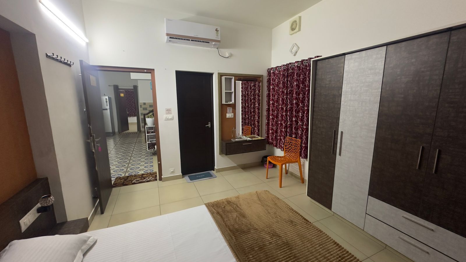 A hotel room with a bed, wardrobe, and a small desk with a chair. There is a door leading to another room and a bathroom.