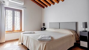 Un dormitorio con cama, mesitas de noche, una ventana con cortinas e instalación de aire acondicionado.