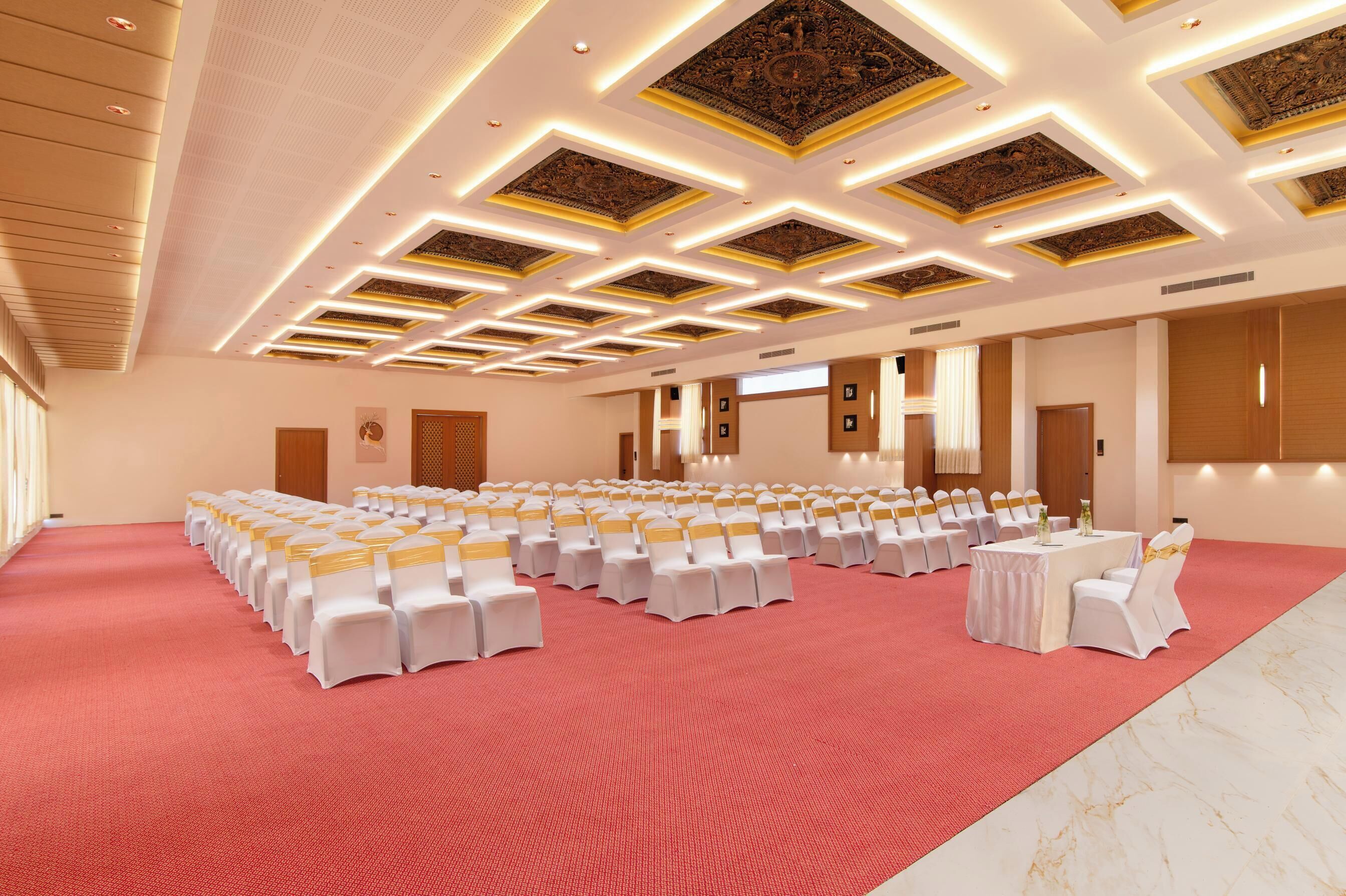 A large conference room with rows of white chairs, a central table, and a red carpet.