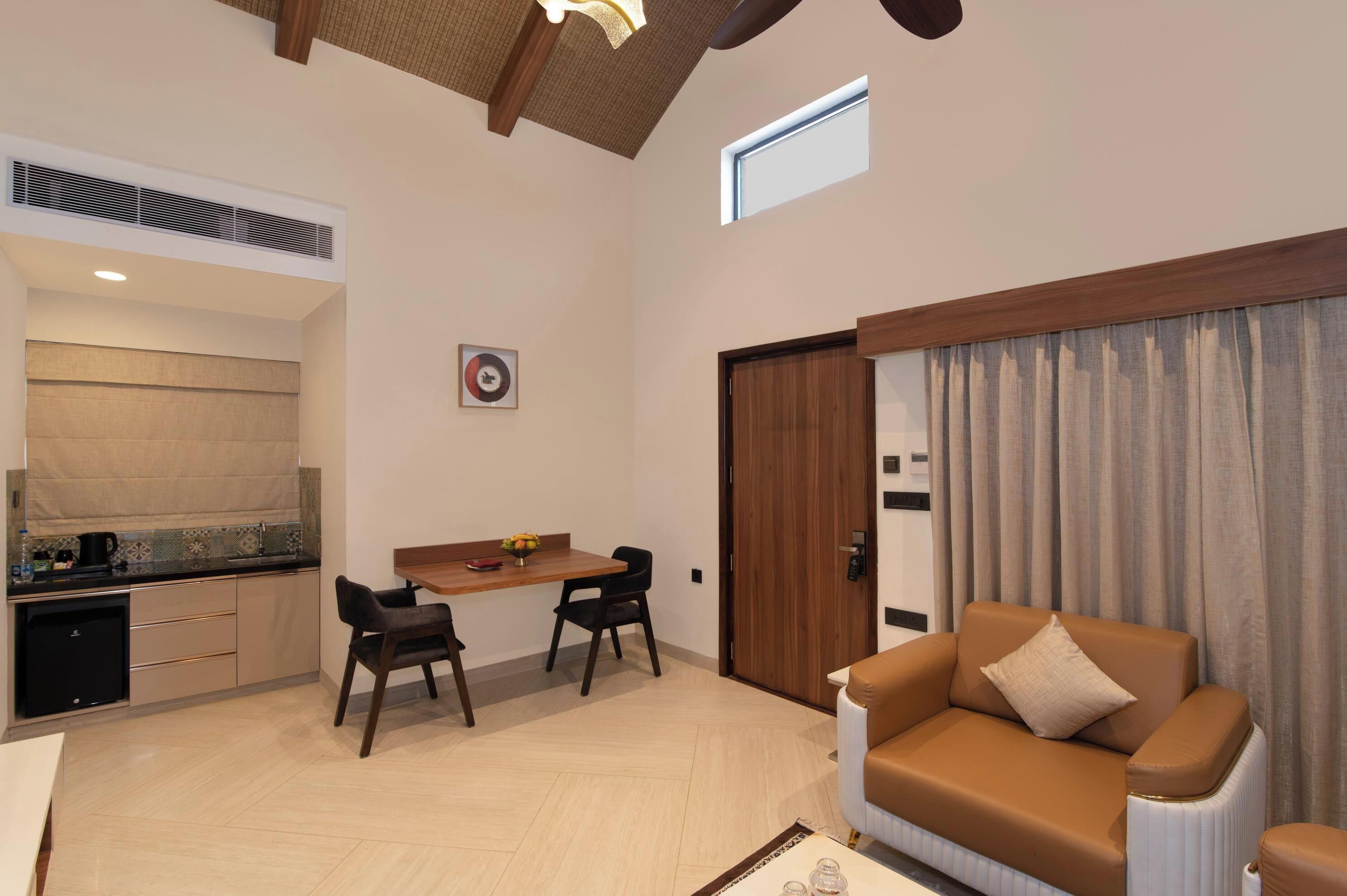 A modern living room with a sofa, a dining area with chairs, a kitchen with a sink, and a window.