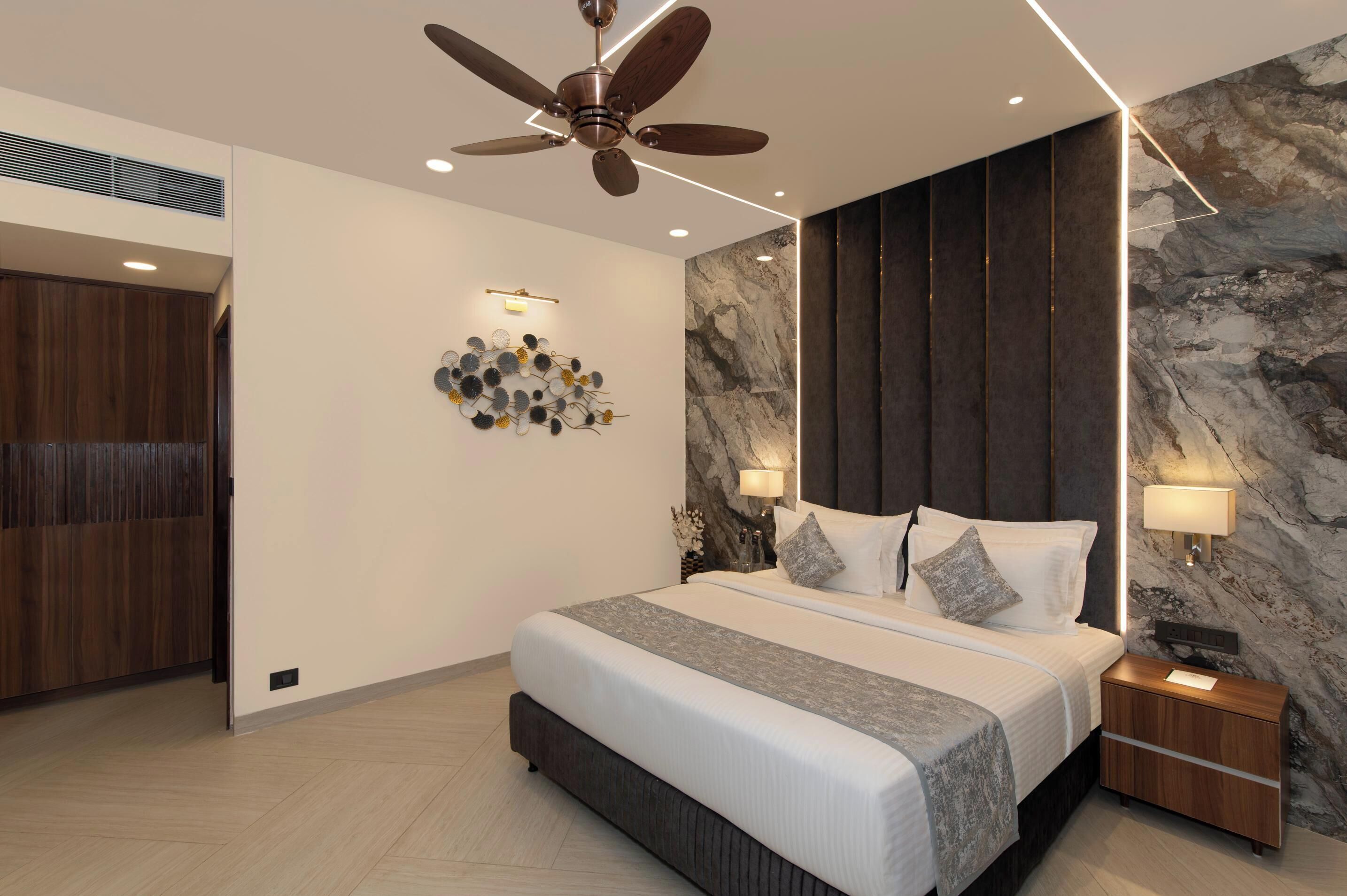 A modern bedroom with a large bed, a ceiling fan, a marble wall, and a wooden wardrobe.
