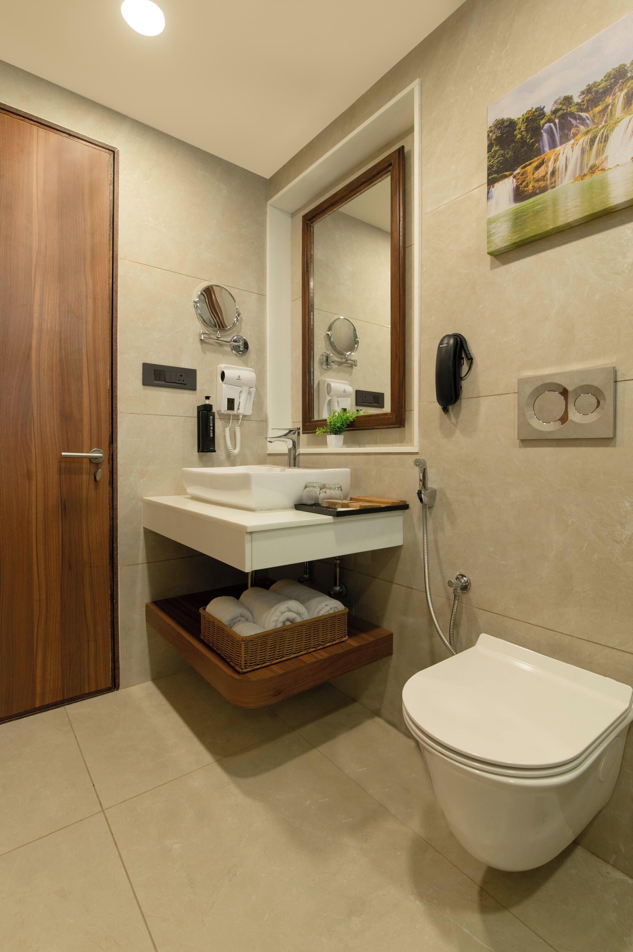 Un baño con puerta de madera, un lavamanos blanco con espejo encima, un inodoro blanco y un teléfono instalado en la pared.