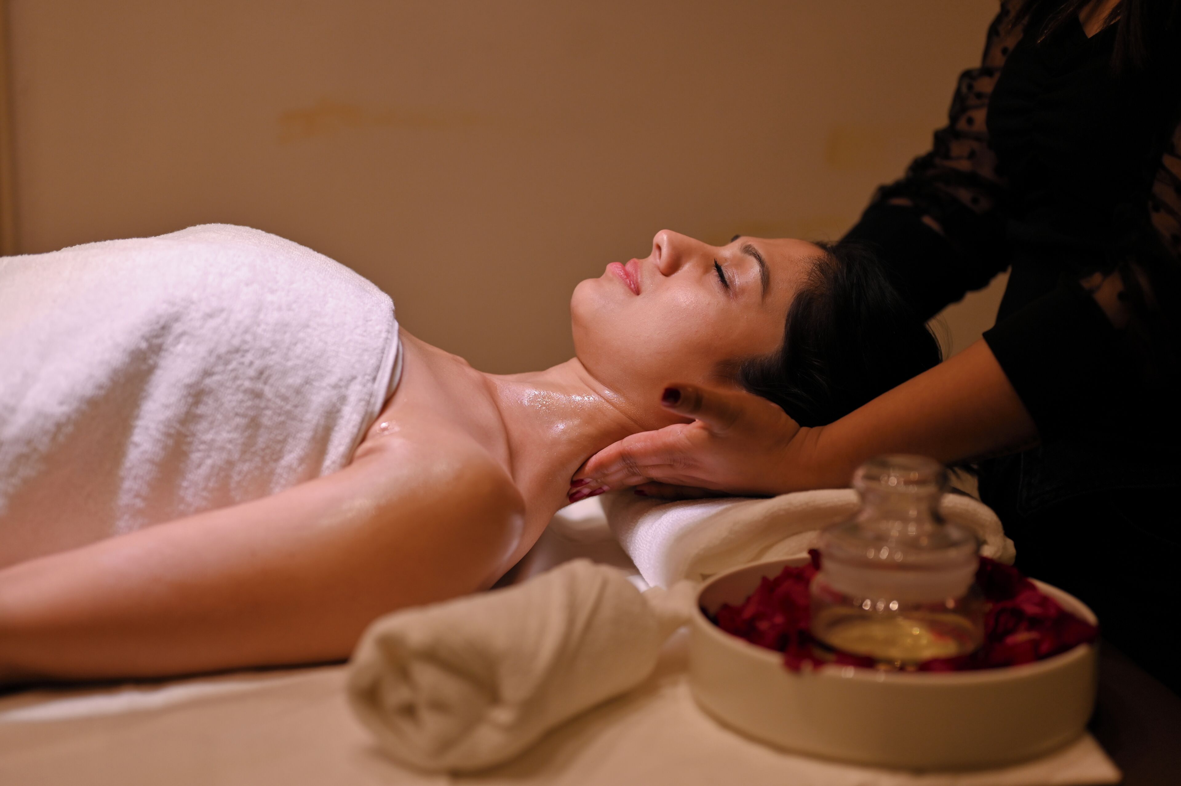 A person receiving a massage with a towel and a bowl of rose petals on a table.