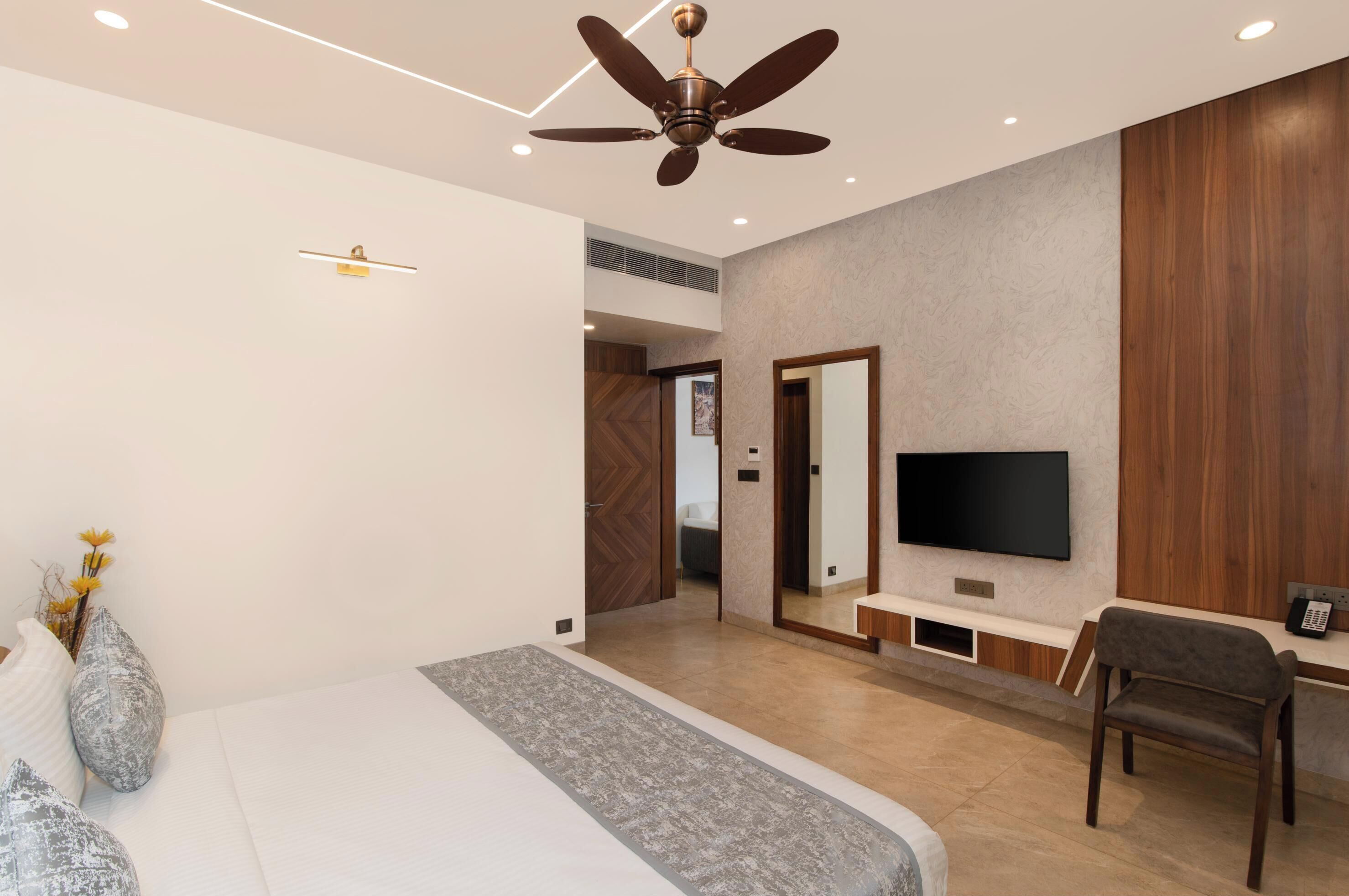 A modern bedroom with a bed, a ceiling fan, a TV, and a desk with a chair.
