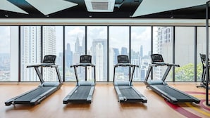 Una palestra con tre tapis roulant allineati, ampie finestre che offrono vista sulla città e una ventola a soffitto.