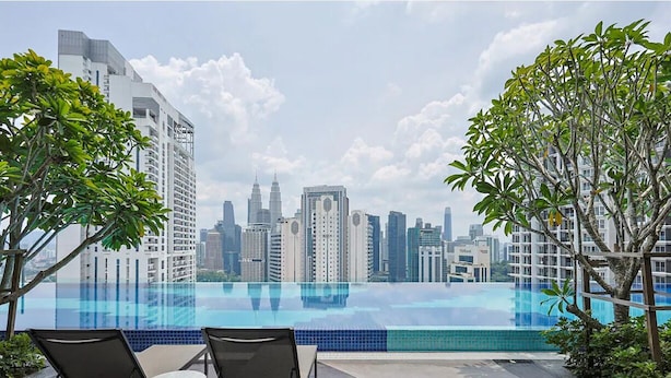 Una piscina a sfioro sul tetto con lettini, immersa nel verde e con vista sullo skyline di una città caratterizzata da edifici moderni.