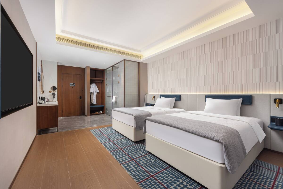 Ein modernes Hotelzimmer mit zwei Betten, einem begehbaren Kleiderschrank, einem Badezimmer und einem großen Spiegel.