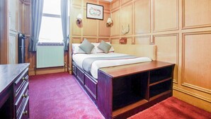 A hotel room with a bed, a dresser, a radiator, a window with curtains, and a wall-mounted picture. - Standard Double Room (Gateshead)