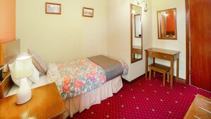 Une chambre à coucher avec un lit, une table de chevet, une lampe, un miroir et un sol recouvert d’une moquette rouge.