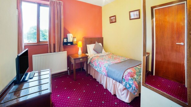 Une chambre d’hôtel comprenant un lit, un bureau, une chaise, un radiateur, une fenêtre avec des rideaux, une lampe et une porte.