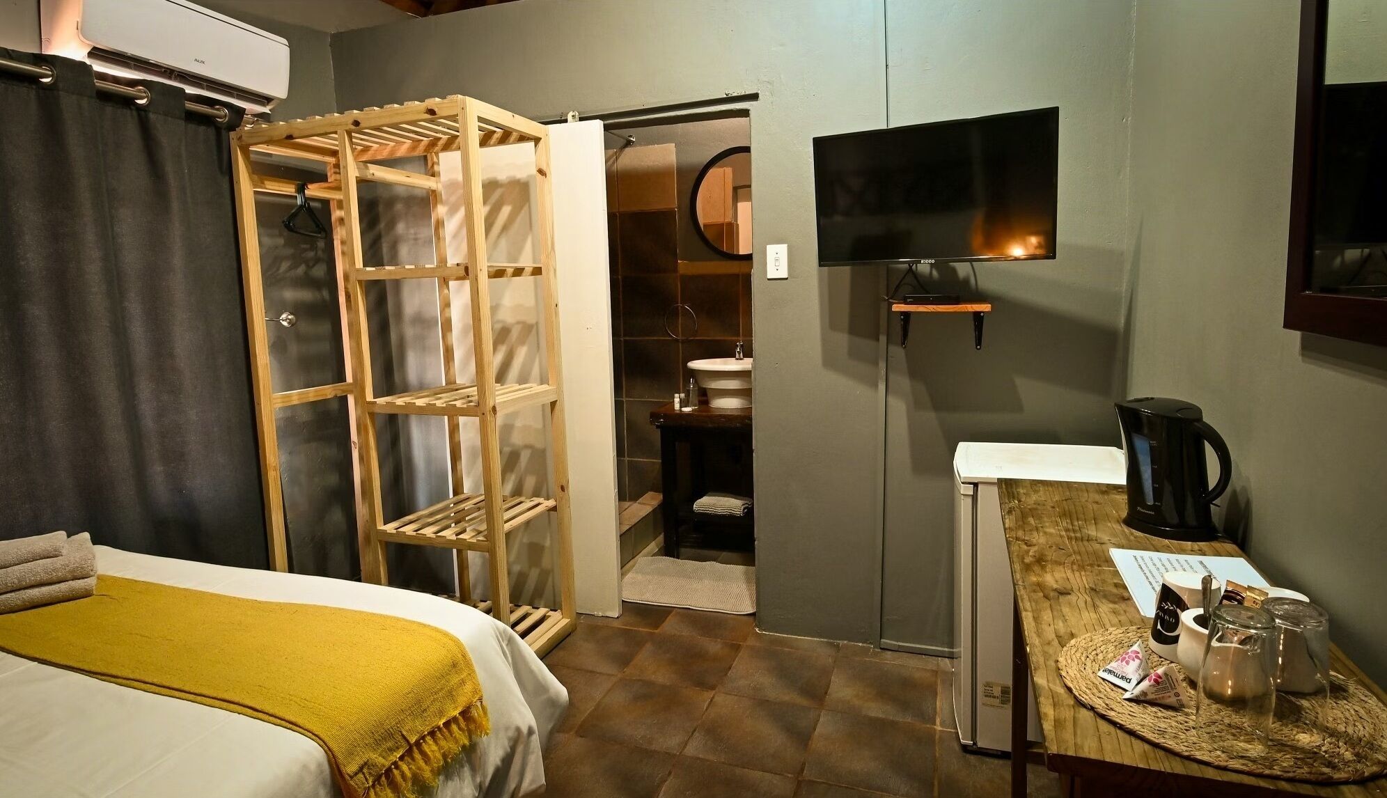 A hotel room with a bed, a desk with a coffee maker, a TV, and a wardrobe with a mirror.