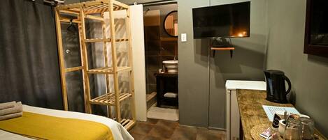 A hotel room with a bed, a desk with a coffee maker, a TV, and a wardrobe with a mirror.