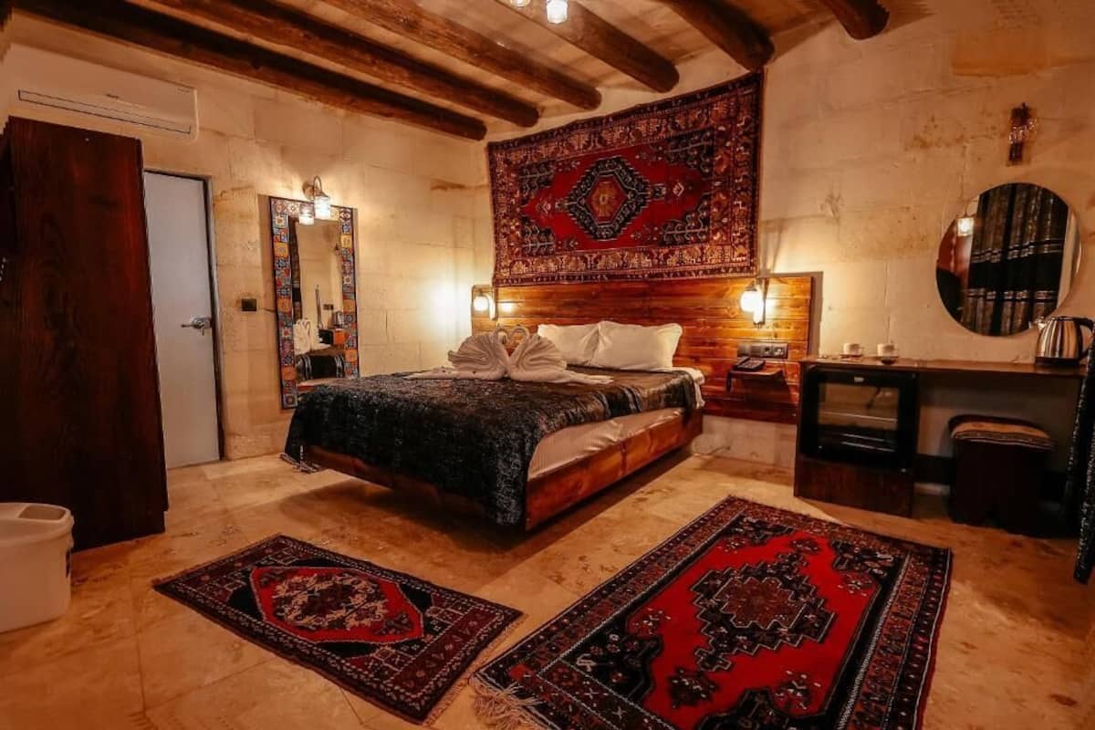 A bedroom with a bed, a wooden headboard, a nightstand, a mirror, a television, and a large tapestry.