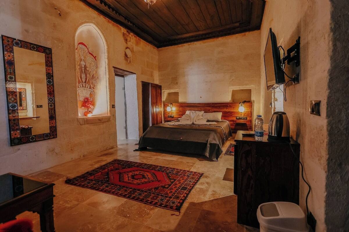 A bedroom with a bed, bedside tables, a mirror, a rug, and a wooden ceiling.