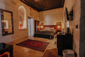 A bedroom with a bed, bedside tables, a mirror, a rug, and a wooden ceiling. - Zümrütü Anka Cave (Ürgüp)