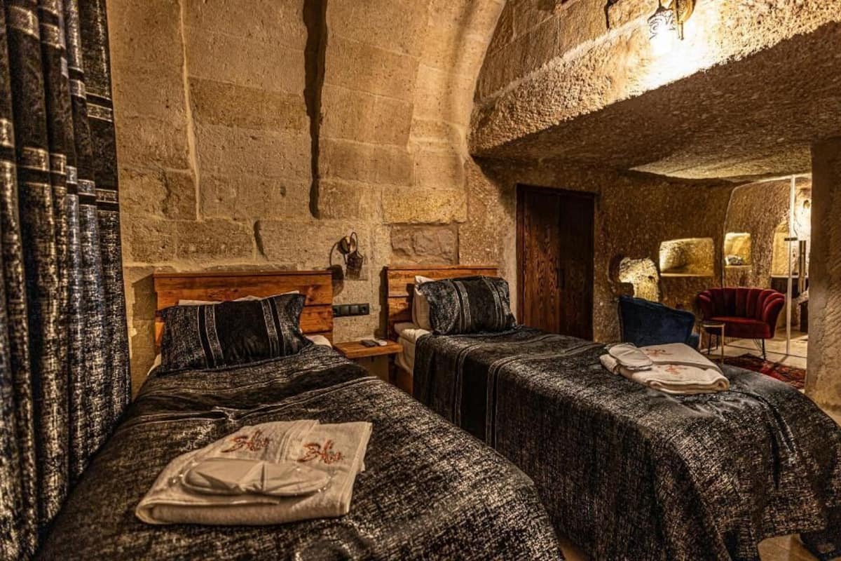 A room with two beds, wooden headboards, and a stone wall.