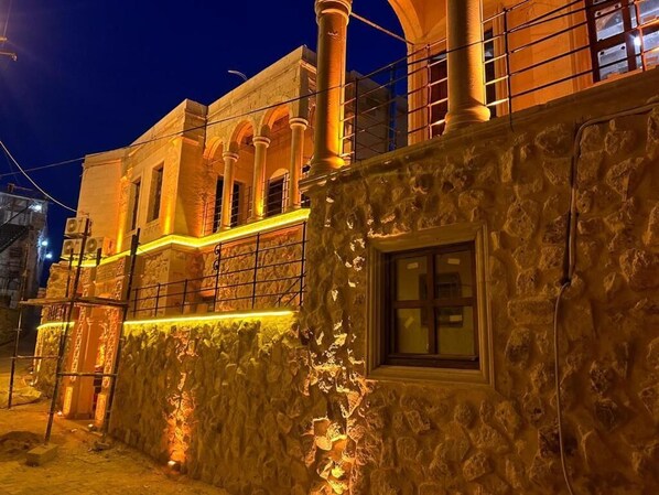 Un edificio de piedra con un balcón y una ventana, iluminado por una luz cálida.