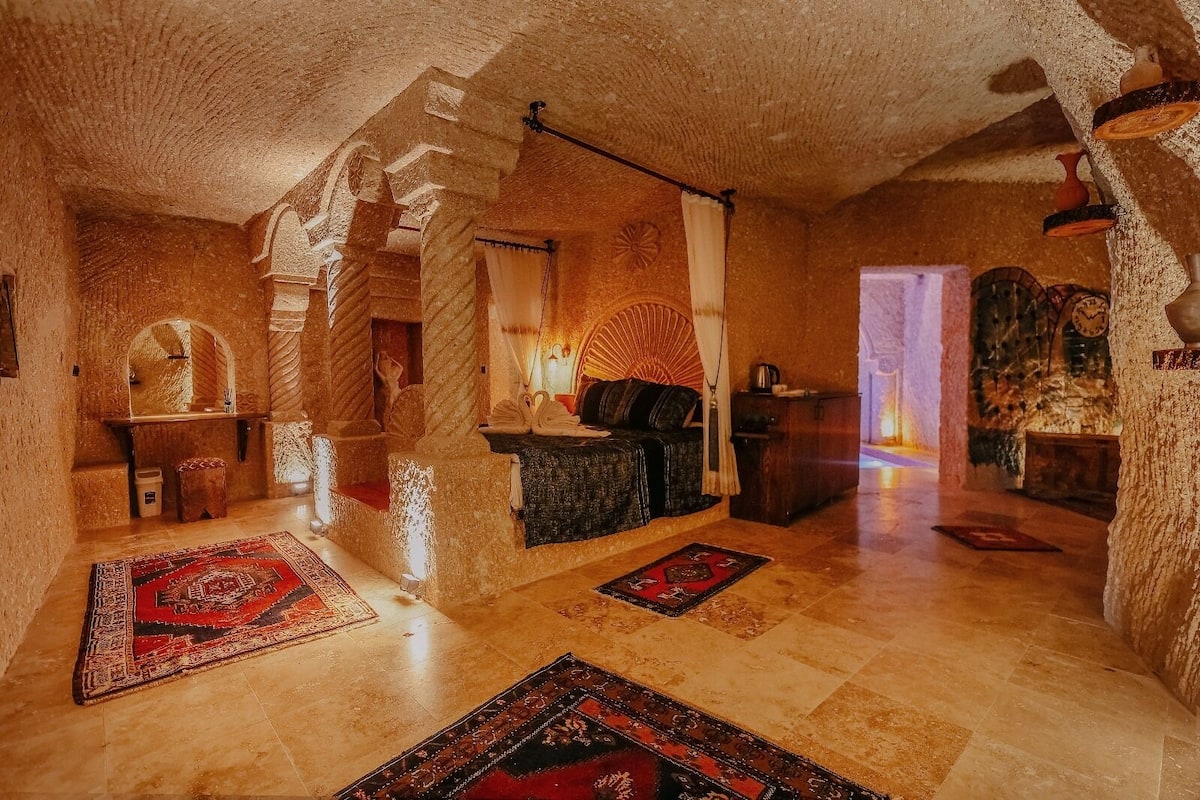 A room with stone walls, a bed, a small table, and a chair.