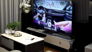 Un salon moderne doté d’un grand téléviseur à écran plat diffusant une vidéo musicale, d’un coin repas avec une table en marbre et d’un espace salon confortable.
